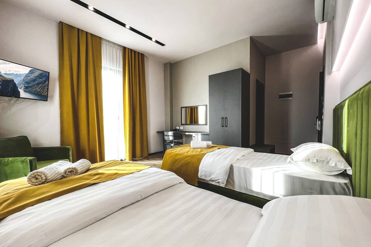 A hotel room with two beds, a desk, a chair, a TV, and a large window with curtains.