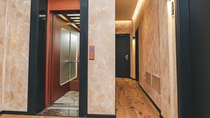 Un pasillo moderno con suelo de madera, un ascensor de cristal y una puerta con marco rojo.