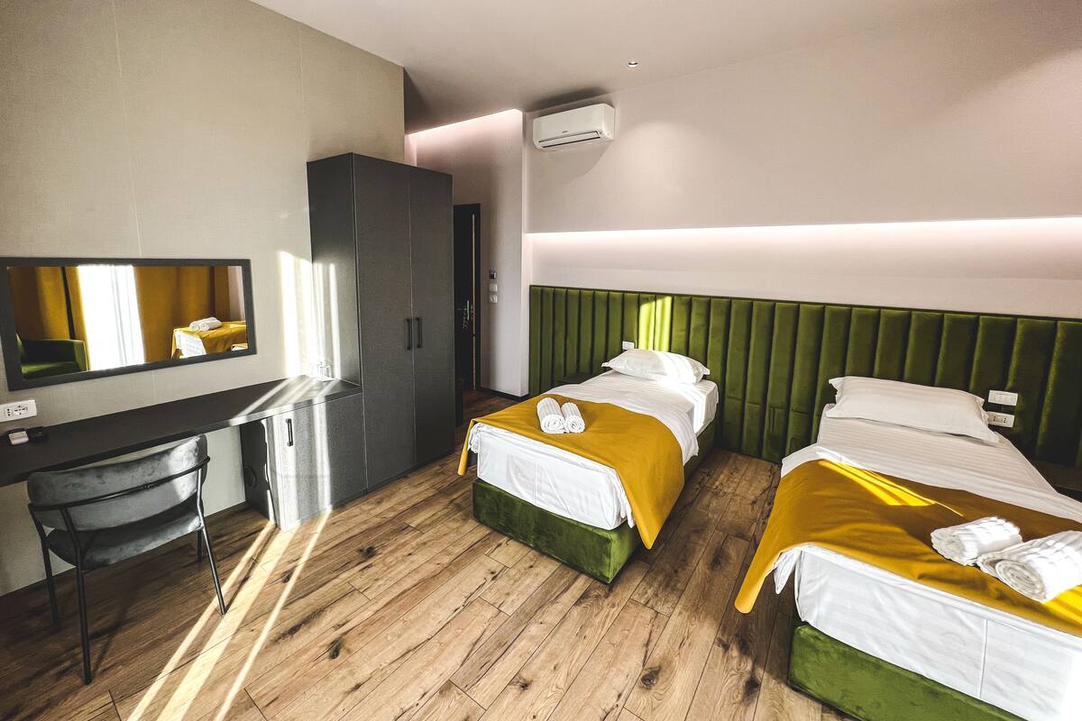 A hotel room with two beds, a desk, and a mirror.