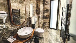 Un baño con pared de mármol, un espejo grande, un lavabo, un inodoro y una ducha.