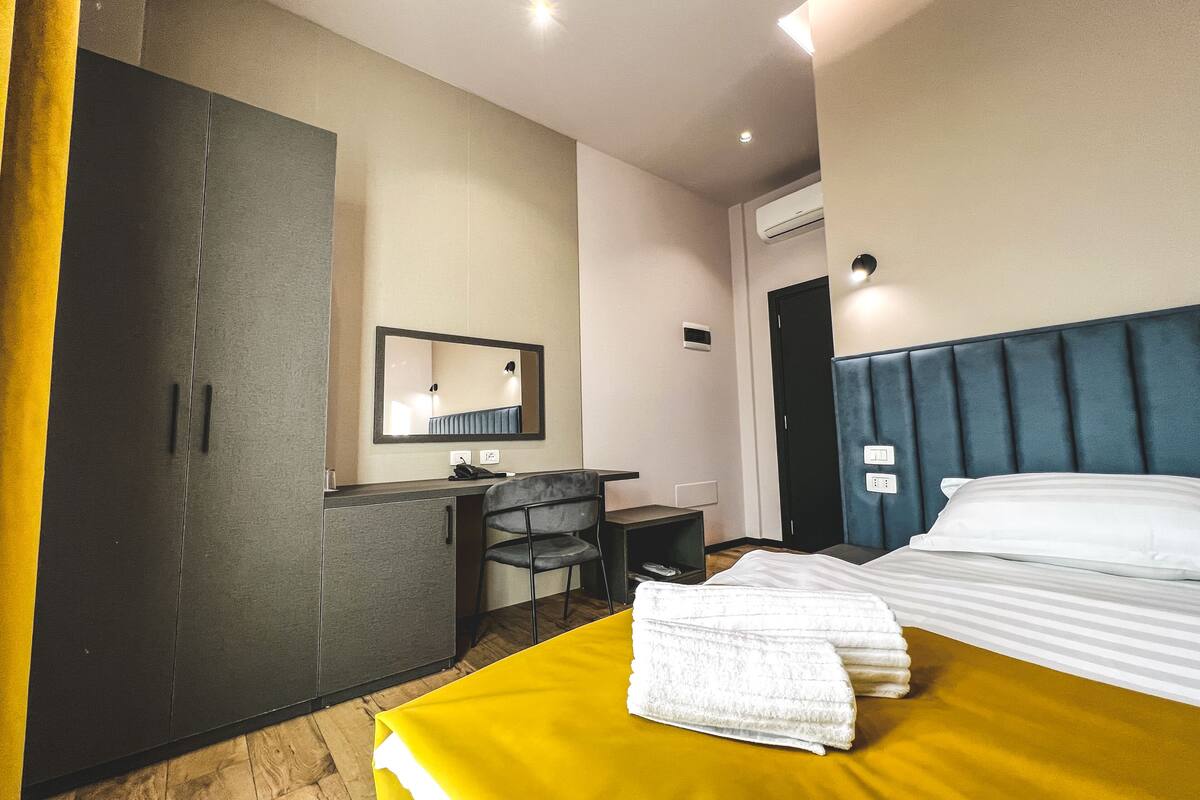 A hotel room with a bed, a desk, a chair, and a wardrobe.