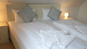 A neatly made bed with white linens, two patterned pillows, and a bedside lamp.