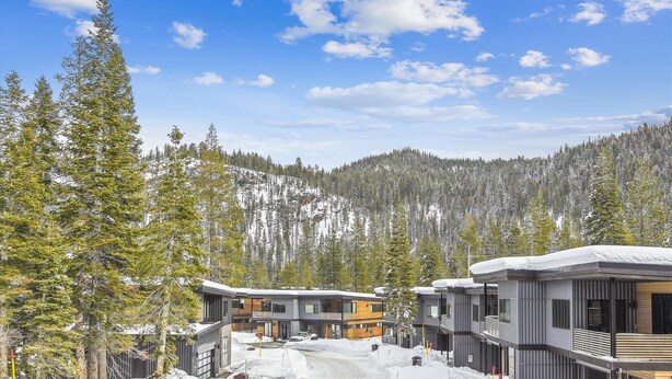 A modern resort with multi-story buildings, a snow-covered landscape, and a forested mountain backdrop. - Diamond Run at Palisades by Tahoe Getaways - Luxury 4BR Townhome, Pet-Friendly, Shuttle & Hot Tub! (Olympic Valley)