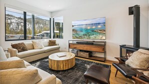 A modern living room with a large TV, comfortable seating, and a fireplace. - Diamond Run at Palisades by Tahoe Getaways - Luxury 4BR Townhome, Pet-Friendly, Shuttle & Hot Tub! (Olympic Valley)