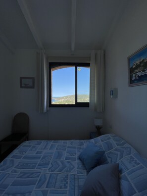 Une chambre à coucher avec un lit, une fenêtre donnant sur un beau paysage, une chaise et une lampe.