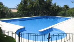 Een rechthoekig zwembad met een blauw binnengedeelte, omgeven door een wit zonnedek en een zwart metalen hek.