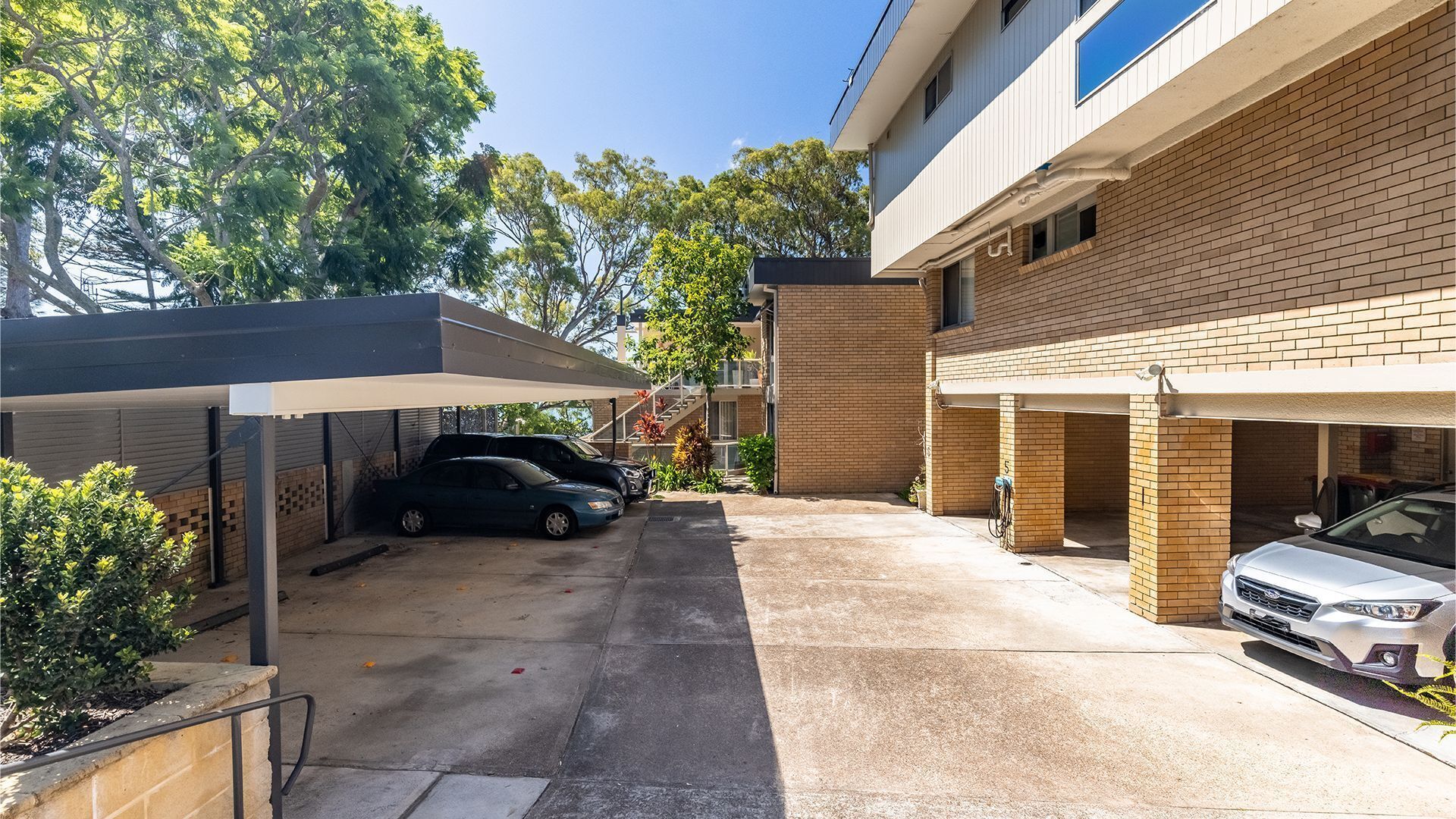 Uma área de estacionamento com carros, uma galeria coberta e um edifício com paredes de tijolo e telhado plano.