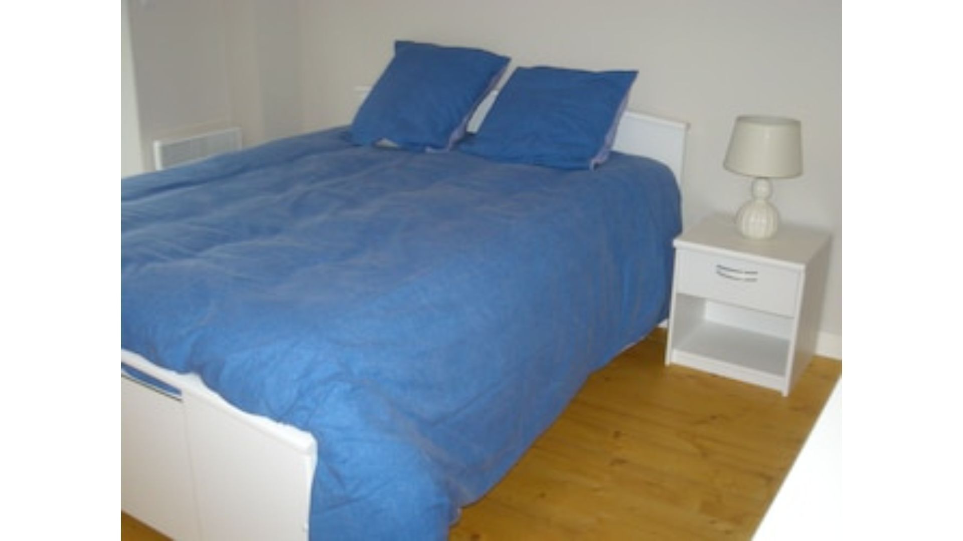 Ein Schlafzimmer mit einem Bett, zwei Kissen, einem Nachttisch mit Lampe und Holzboden.