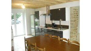 A modern kitchen with a large island, built-in appliances, and a dining area with wooden chairs. - Grand Gite 15 pers. Saint Malo / Cancale Le Mont Saint Michel Le Noisetier (Baguer Pican)