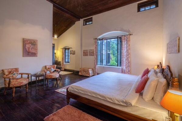 Un dormitorio con una cama grande, dos sillas, una mesita y una ventana con cortinas.
