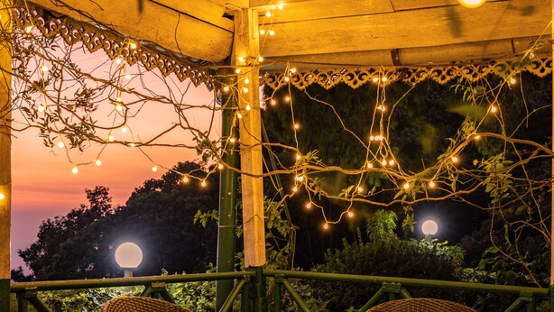 Une terrasse extérieure avec des chaises et des tables en osier, des guirlandes lumineuses et une vue sur la lune.