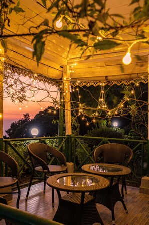 An outdoor patio with wicker chairs and tables, string lights, and a view of the moon. - Amã Stays & Trails Wayside, Kurseong (Kurseong)