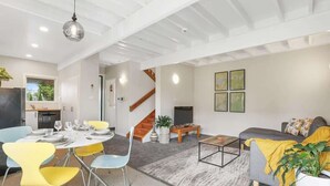 Una sala de estar moderna con comedor, una escalera y una cocina visible al fondo.