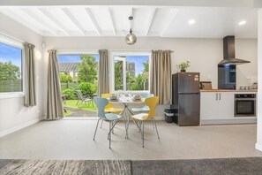 A modern kitchen with a dining area, large windows, and a view of the outdoors. - Papawai Townhouse 11 - Walk to Town, Sleeps 4 (Rotorua)