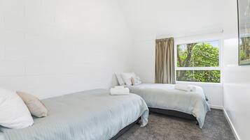 Ein Hotelzimmer mit zwei Einzelbetten, einem Fenster mit Vorhängen und Blick auf Grünflächen.