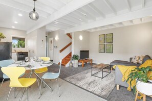 A modern living space with a dining area, a sofa, a coffee table, and a staircase. - Papawai Townhouse 11 - Walk to Town, Sleeps 4 (Rotorua)