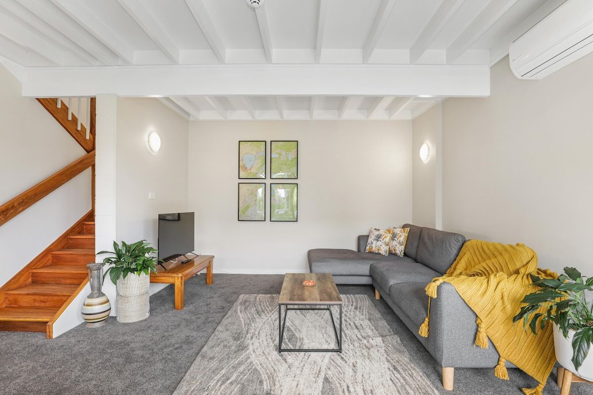 A modern living room with a grey sofa, a coffee table, and a staircase.