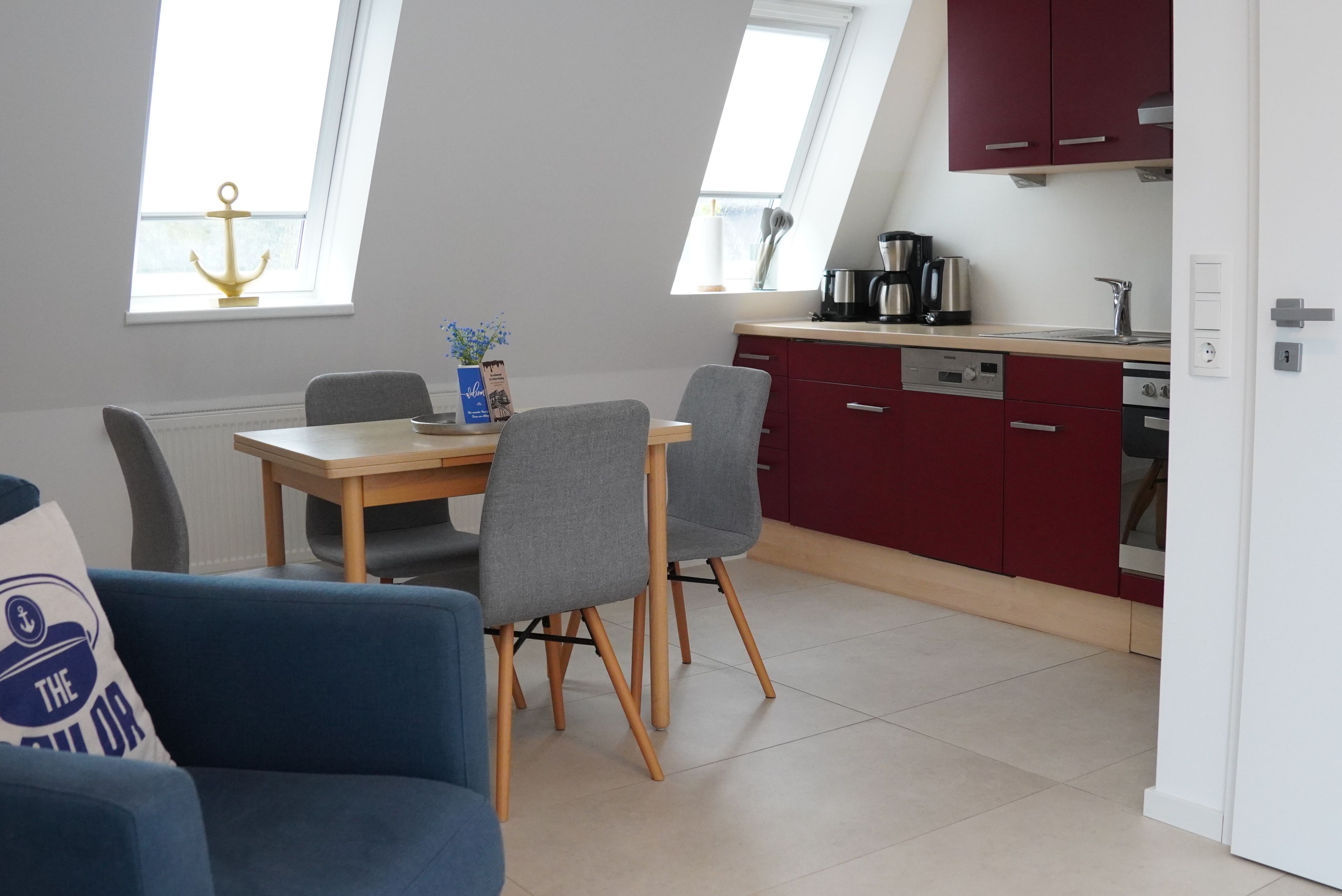 Une cuisine moderne avec des meubles de rangement rouges, une table à manger avec des chaises et une machine à café.