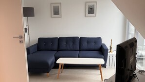 Een moderne woonkamer met een donkerblauwe modulaire bank, een witte salontafel en een flatscreen televisie op een meubel.