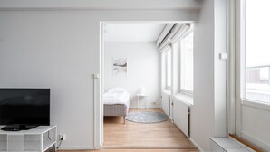 A modern, minimalistic bedroom with a bed, bedside table, and a TV on a white stand. - 1BR with Sauna, Rooftop Terrace & Amazing Views (Tampere)