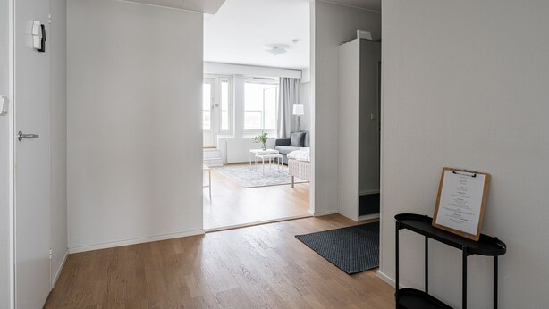 A modern hotel room with a wooden floor, a small rug, a desk with a clipboard, and a view into the living area. - 1BR with Sauna, Rooftop Terrace & Amazing Views (Tampere)