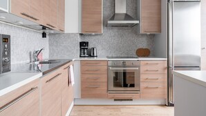 A modern kitchen with wooden cabinets, a stainless steel refrigerator, and a built-in oven. - 1BR with Sauna, Rooftop Terrace & Amazing Views (Tampere)