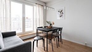 A modern living room with a sofa, dining table, and chairs. There is a window with curtains, a framed artwork on the wall, and a small plant on the table. - 1BR with Sauna, Rooftop Terrace & Amazing Views (Tampere)