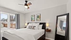 Ein Schlafzimmer mit einem Bett, einem Deckenventilator, zwei Wandlampen, einem großen Spiegel und einem Fenster mit Vorhängen.