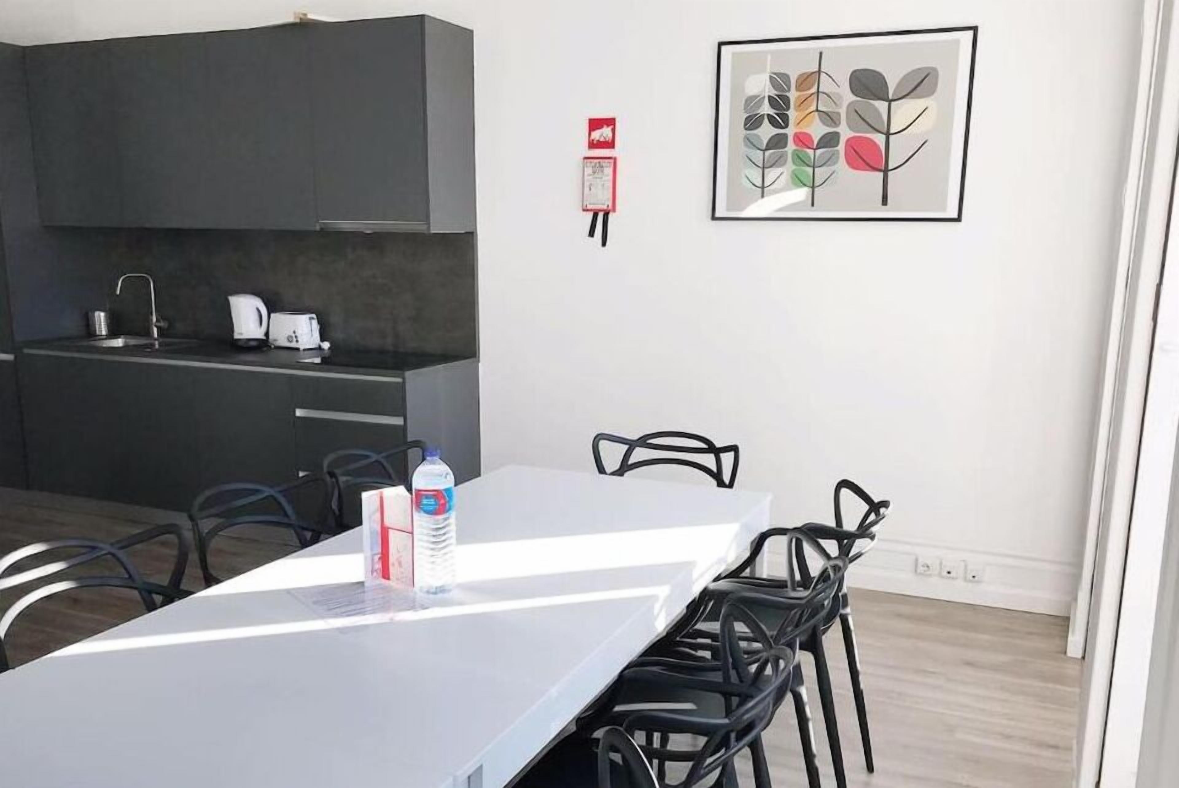 A modern kitchen with dark cabinets, a white countertop, and a sink. There is a framed artwork on the wall and a fire extinguisher mounted on the wall.