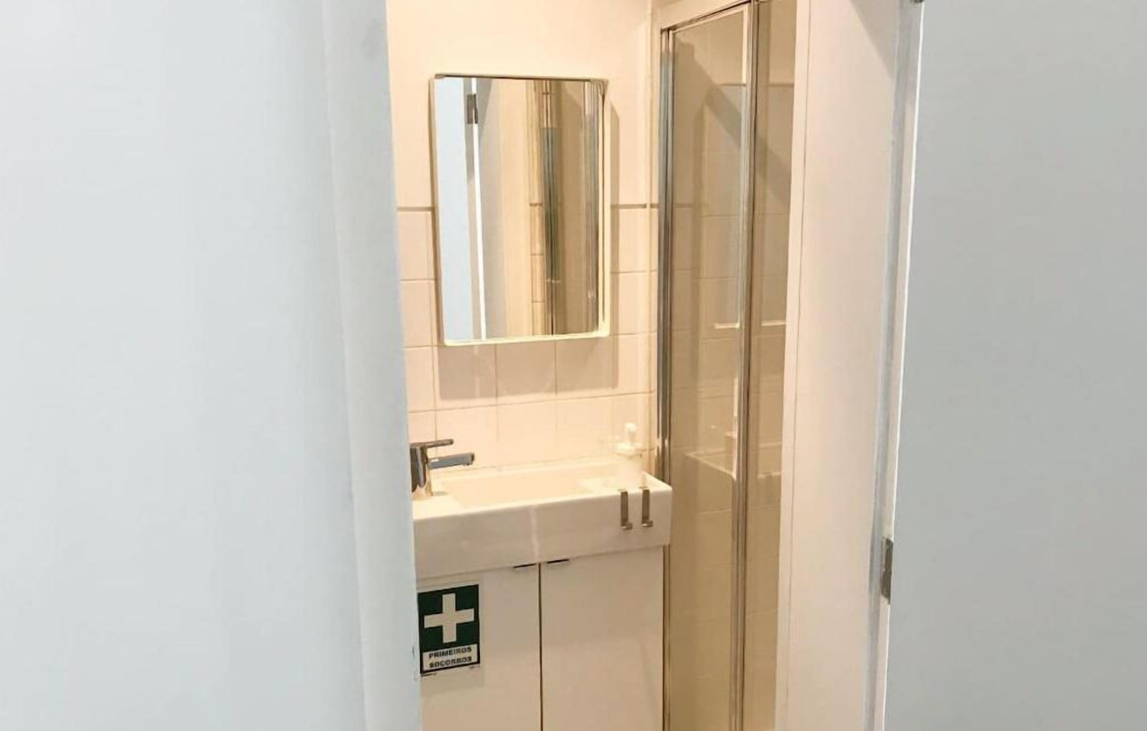 A small bathroom with a glass shower enclosure, a sink with a mirror, and a sign indicating first aid availability.