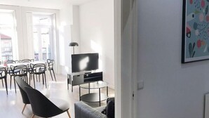 A modern living room with a TV, a round coffee table, and a sofa. There is a dining area with chairs and a table in the background. - Downtown Fantail (Porto)