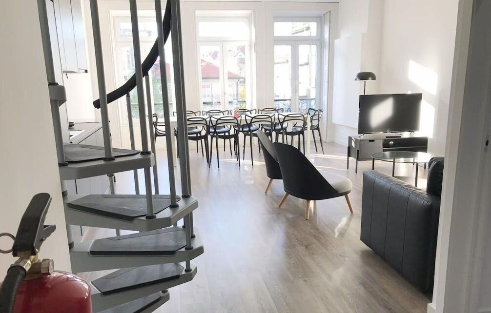 Uma sala de estar moderna com escada, televisão de tela plana e área de jantar com cadeiras e mesas.