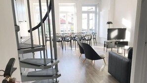 A modern living room with a staircase, a flat-screen TV, and a dining area with chairs and tables. - Downtown Fantail (Porto)