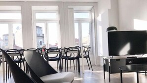 A modern living room with a large TV, black and grey furniture, and large windows offering a view of buildings outside. - Downtown Fantail (Porto)