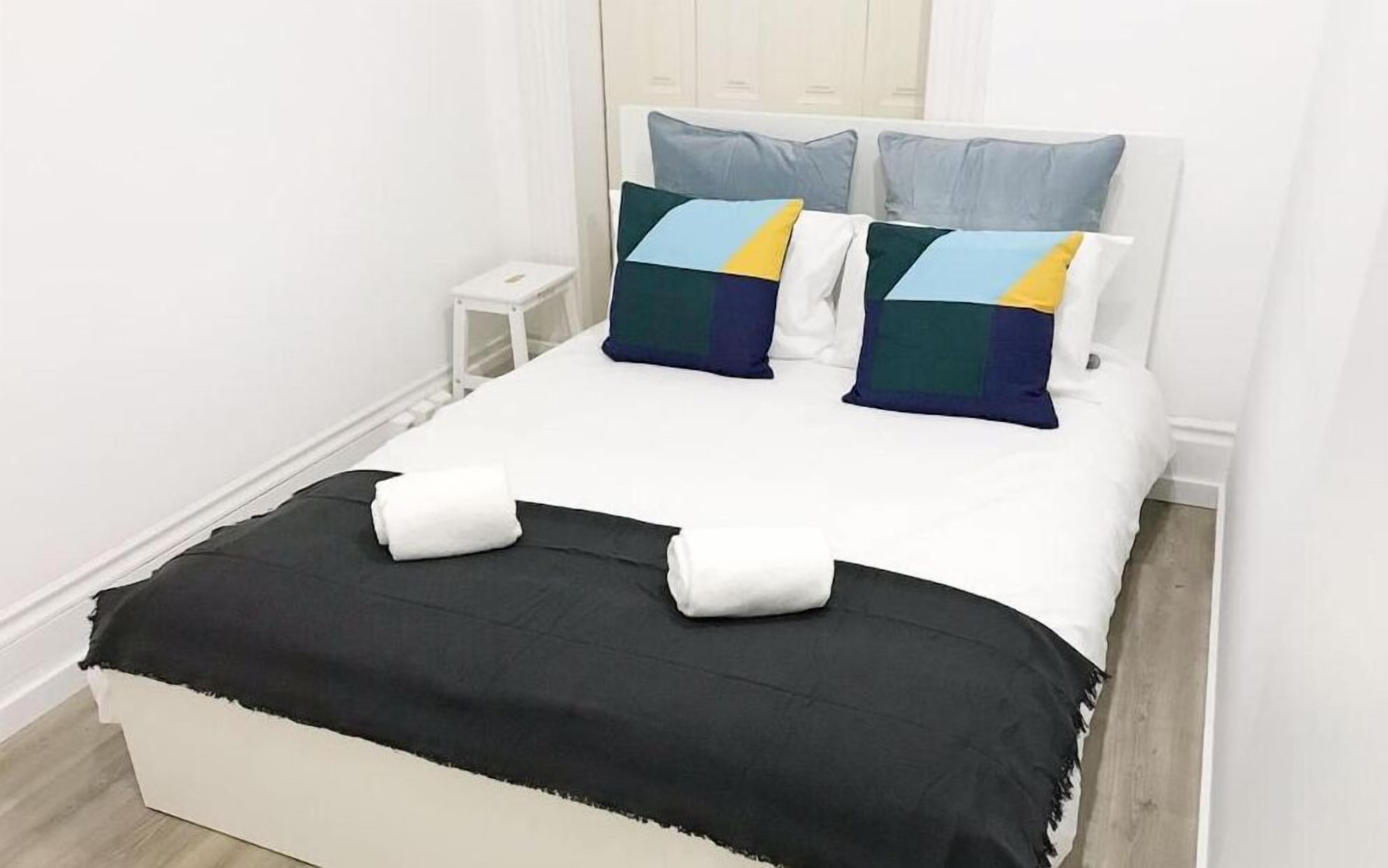 A neatly made bed with a black and white bedspread, two pillows with a geometric pattern, and a white nightstand beside it.