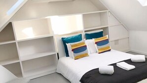 A bedroom with a sloped ceiling, built-in shelving, a bed with colorful pillows, and a skylight. - Downtown Fantail (Porto)