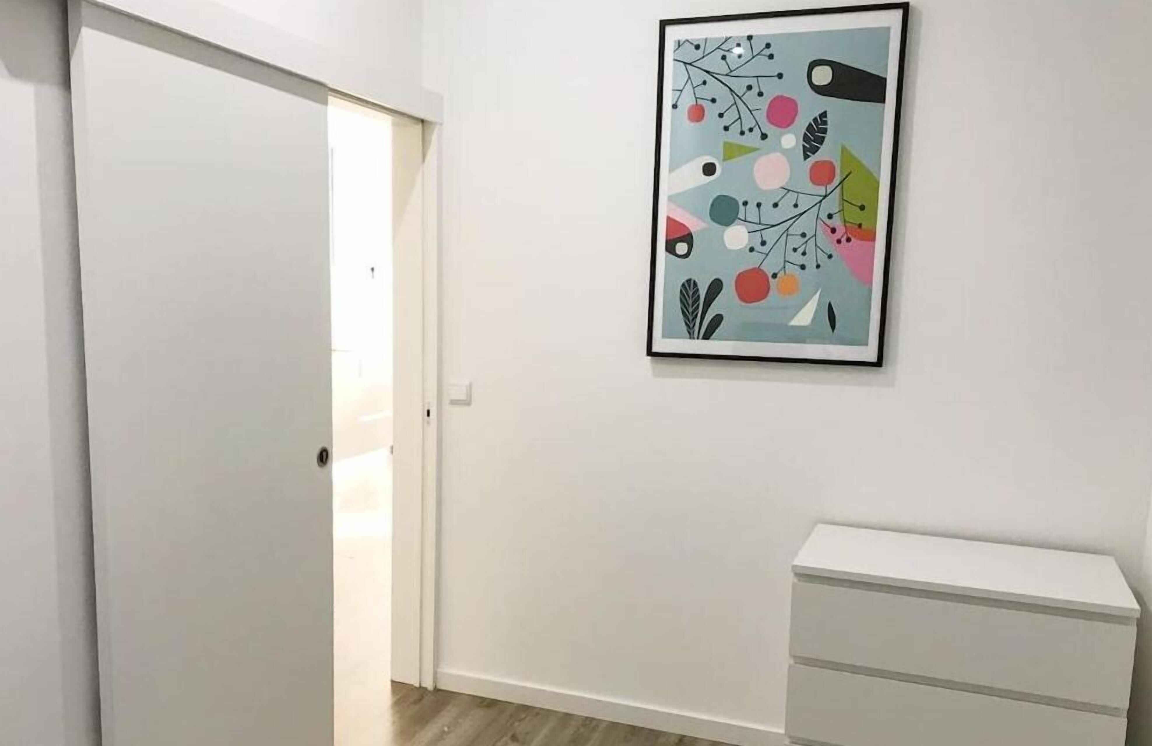 A room with a white door, a white dresser, and a colorful abstract painting on the wall.
