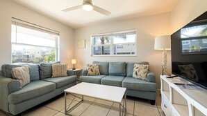 A living room with a sectional sofa, a white coffee table, a ceiling fan, and a TV on a stand. - Cozy 2-bed, 1-bath second-floor unit minutes from Indian Rocks Beach. Sleeps eight with full kitchen, WiFi, smart TV, beach gear, parking, and direct pool access. A comfortable, convenient stay for families and groups (Indian Rocks Beach)