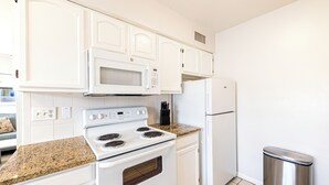 A kitchen with white cabinets, a white stove, a microwave, and a stainless steel trash can. - Cozy 2-bed, 1-bath second-floor unit minutes from Indian Rocks Beach. Sleeps eight with full kitchen, WiFi, smart TV, beach gear, parking, and direct pool access. A comfortable, convenient stay for families and groups (Indian Rocks Beach)