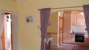A room with a wooden floor, a bed, a chair, a table with a newspaper, a kitchen area with wooden cabinets and a stove, and a door with a curtain. - Vacation apartment Schmitt, Abtsteinach, Odenwald, approx. 25 km to Heidelberg (Abtsteinach)
