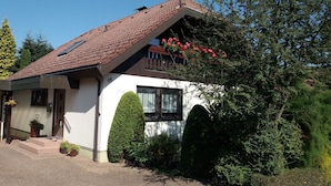 A house with a sloped roof, a small porch, and a garden with potted plants and a flower bed. - Vacation apartment Schmitt, Abtsteinach, Odenwald, approx. 25 km to Heidelberg (Abtsteinach)