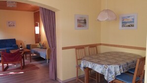 A cozy living room with a blue sofa, a small table with a bottle, and a dining area with a table covered in a patterned tablecloth and wooden chairs. - Vacation apartment Schmitt, Abtsteinach, Odenwald, approx. 25 km to Heidelberg (Abtsteinach)