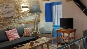 A cozy living room with a stone wall, a sofa, a coffee table, a lamp, a TV, and a staircase. - Beautiful town house in San Jordi, Castellón (Sant Jordi)
