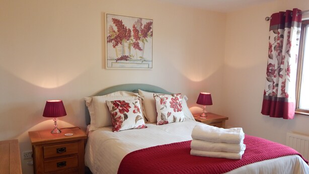 Une chambre à coucher avec un lit, deux tables de chevet, une commode, une lampe, une fenêtre avec des rideaux et un tableau au mur.