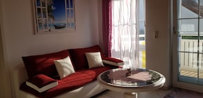 Ein rotes Sofa mit weißen Kissen, ein Glastisch und ein Bild von einem Boot am Strand.