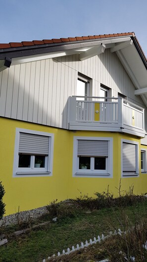 Ein zweistöckiges Gebäude mit gelbem Mauerwerk, weißen Fensterläden und einem Balkon mit weißer Brüstung.
