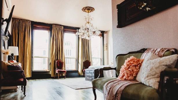 A room with a green sofa, a red chair, a chandelier, and large windows with curtains. - Spacious and Elegant Condo in Downtown Hillsboro (Hillsboro)