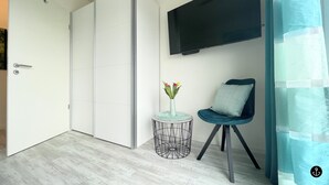 A modern room with a wardrobe, a round side table with a vase, a chair, and a mounted TV. - Sonnenweg 36 - LAKEVIEW HOUSE TÜRKIS (Diemelsee)