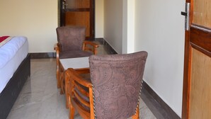 A hotel room with a bed, a dining table with chairs, a television mounted on the wall, and a wooden door. - Hotel Lake Paradise Inn (Nainital)