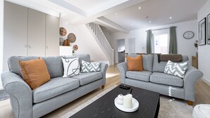Un salon moderne avec deux canapés gris, une table basse noire et un escalier menant à un niveau supérieur.